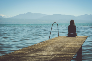 Woman sitting woman sitting on the edge of the footbridge and looking at the lake. How to deal with sadness? Mindletic Blog