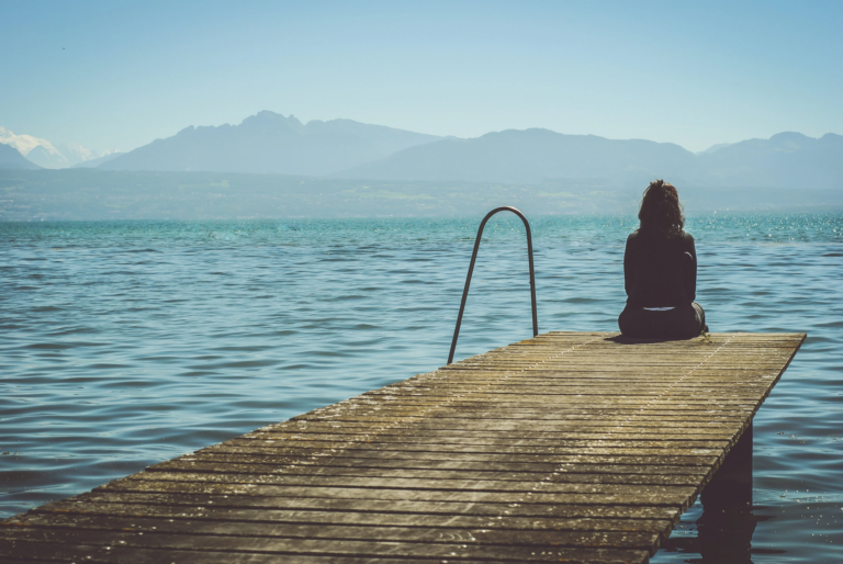 Woman sitting woman sitting on the edge of the footbridge and looking at the lake. How to deal with sadness? Mindletic Blog
