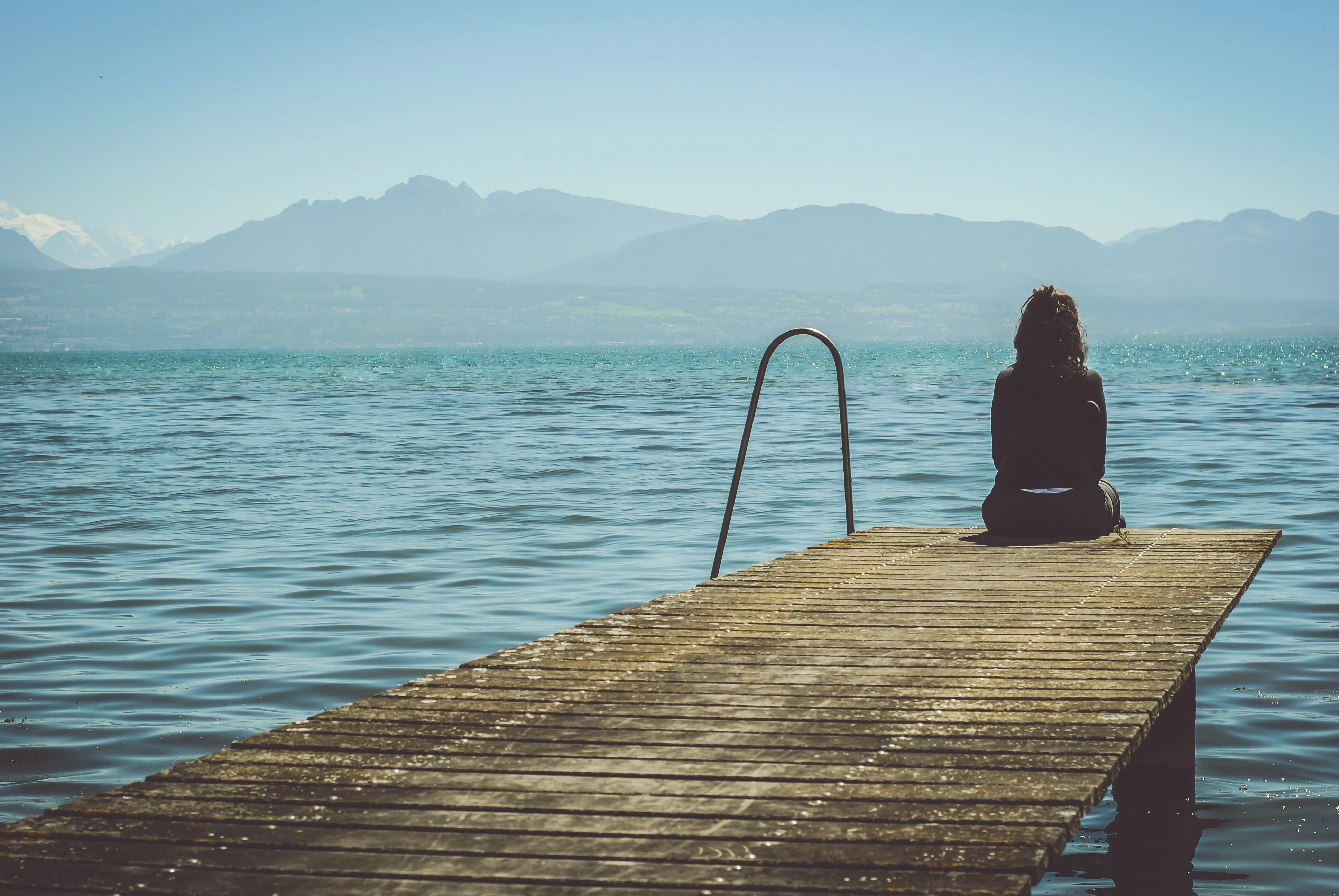 Woman sitting woman sitting on the edge of the footbridge and looking at the lake. How to deal with sadness? Mindletic Blog