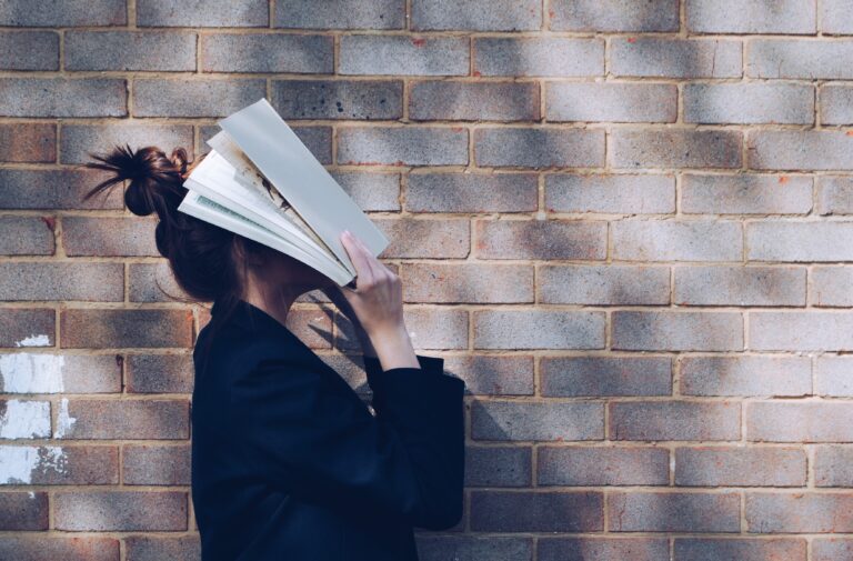 Woman hiding face with a book. Psychological roots and ways to overcome procrastination. Mindletic blog