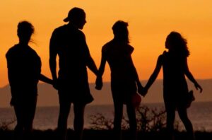 A joyful family gathers together, silhouetted against the warm hues of a vibrant sunset. Parents and children share laughter, sitting on a blanket spread across the grass. The sun's golden glow bathes the scene, creating a serene atmosphere as the family embraces the beauty of the moment.